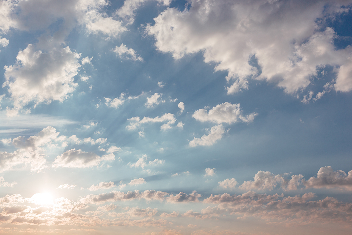 Pale blue sky with white clouds and the sun in the distance.