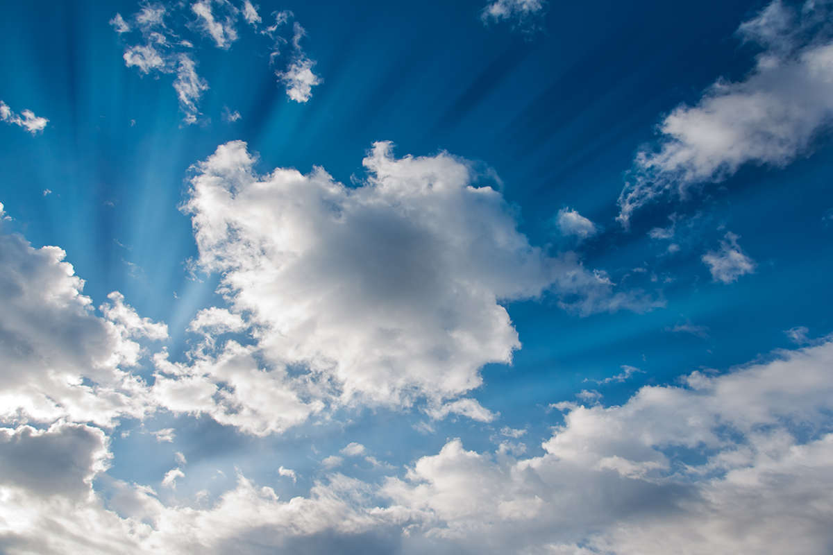 Deep blue sky with white clouds and a light burst from the sun.