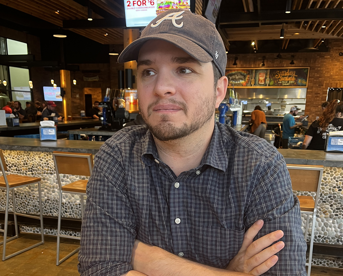 Michael Foster poses at a restaurant while wearing an Atlanta Braves hat.