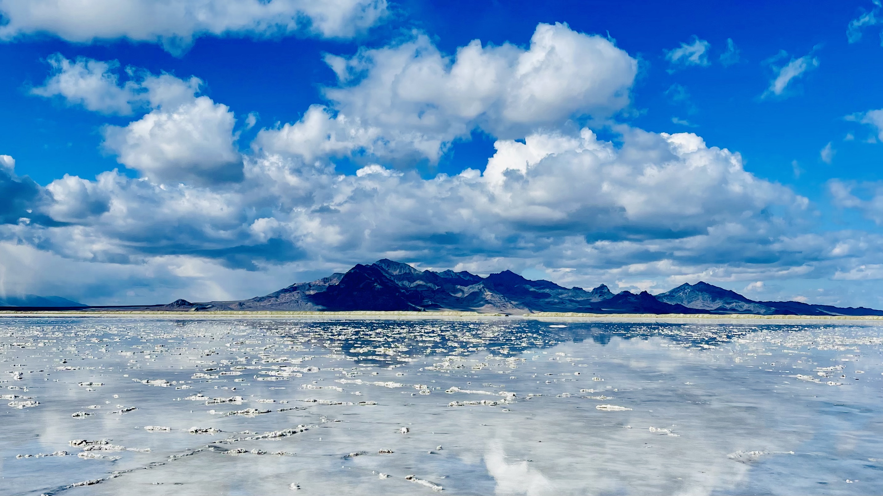 Photo of sky with clouds, with a mountaintop in the distance next to the beach.
