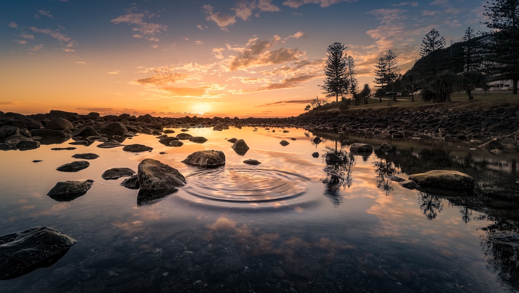 Lake with rocks along the shore and a sunset in the distance.